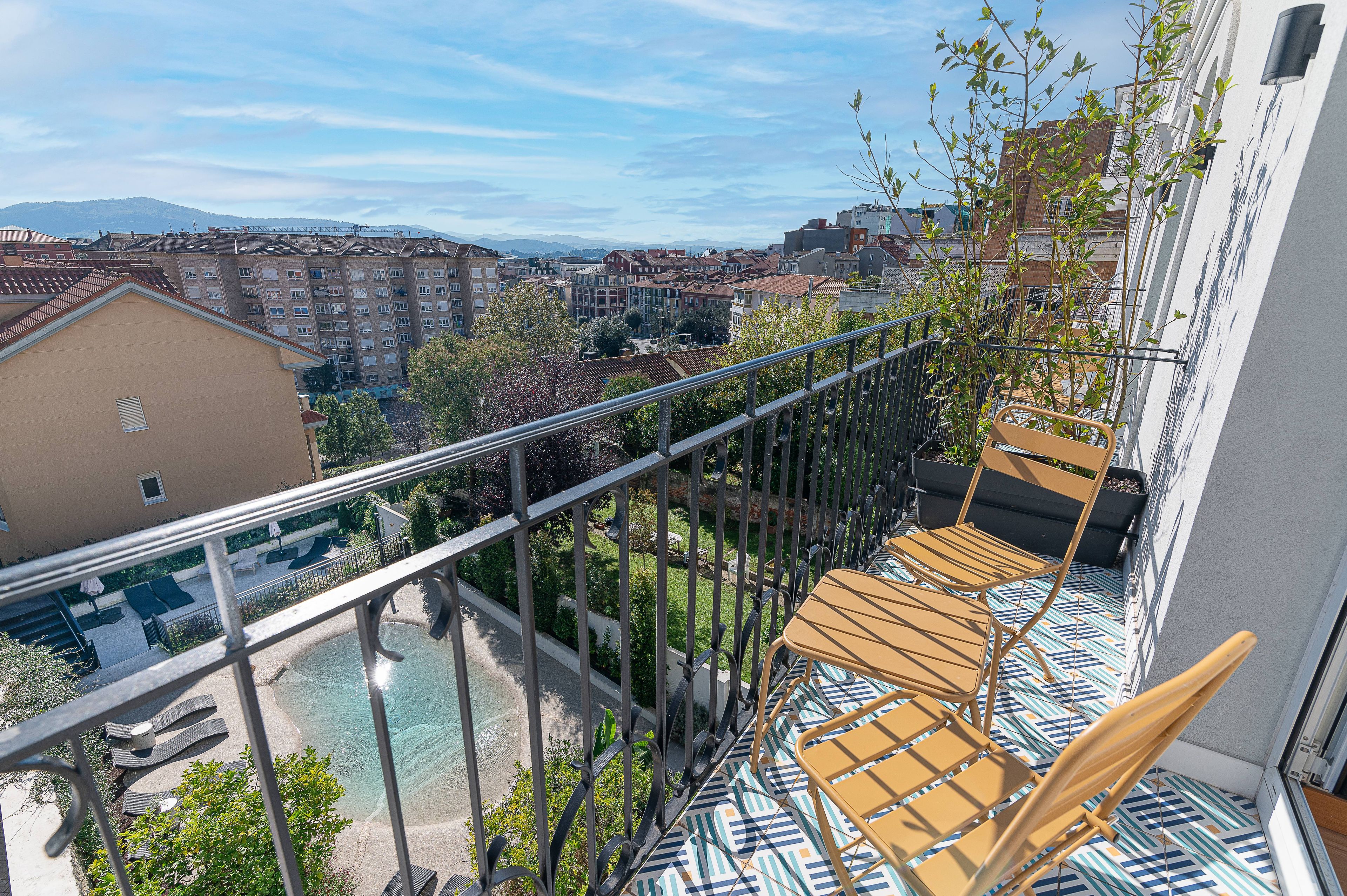 Un balcón con vista a una piscina, un paisaje urbano y una cadena montañosa.