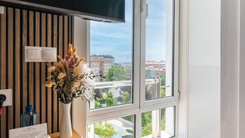 Ein Hotelzimmer mit großem Fenster, einem Flachbildfernseher, einer Vase mit Trockenblumen und einer Wandpaneele aus Holz.