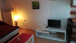 A hotel room with a bed, a TV on a white stand, a red rug, a lamp, and a wall-mounted air conditioner. - Studio Rakella (Opatija)