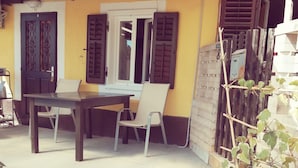 A covered outdoor seating area with a table and chairs, a potted plant, and a door with a decorative design. - Studio Rakella (Opatija)