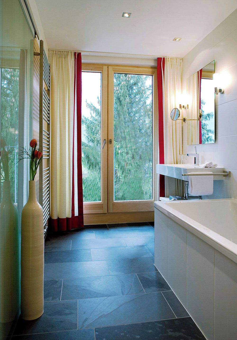 Ein Badezimmer mit Badewanne, Waschbecken, Spiegel und einem Fenster mit Vorhängen.