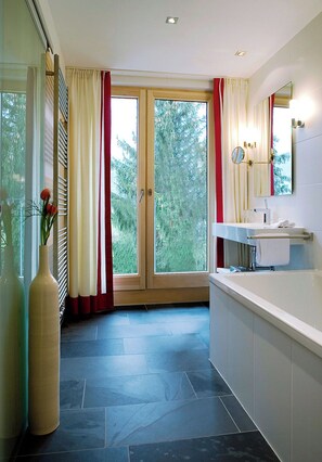 Un baño con bañera, lavabo, espejo y ventana con cortinas.