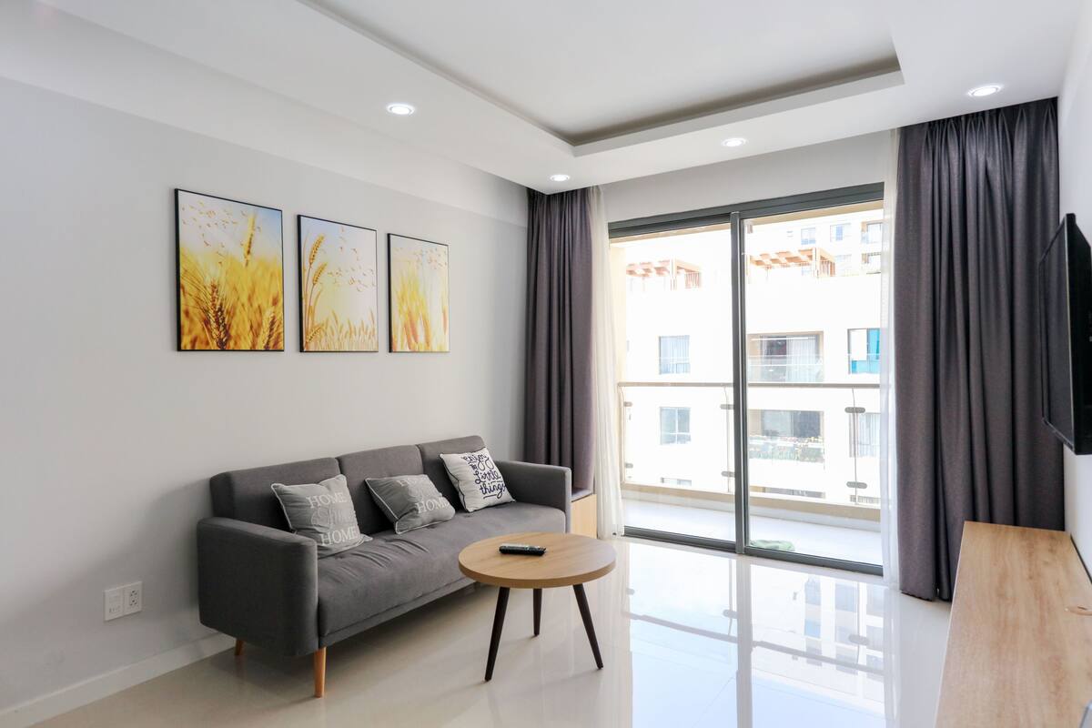 A modern living room with a grey sofa, a round wooden coffee table, and three framed artworks on the wall.