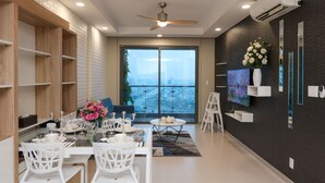 Un espace repas moderne avec une table en verre, des chaises blanches et une vue sur la ville grâce à de grandes fenêtres.
