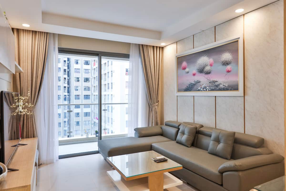 A modern living room with a sofa, a glass coffee table, and a large window with curtains.