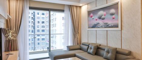 A modern living room with a sofa, a glass coffee table, and a large window with curtains.