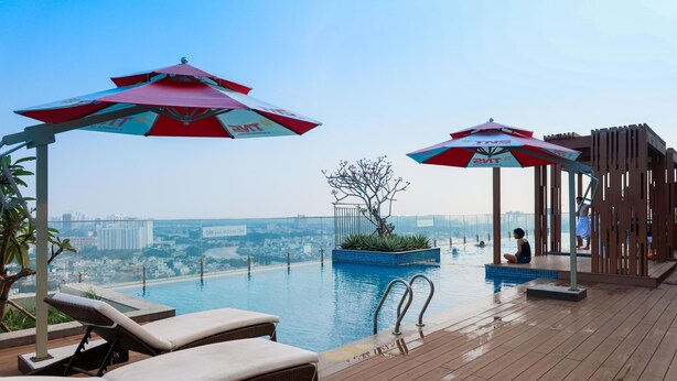 Une piscine à débordement située sur le toit, dotée de chaises longues et de parasols, et offrant une vue sur le paysage urbain.