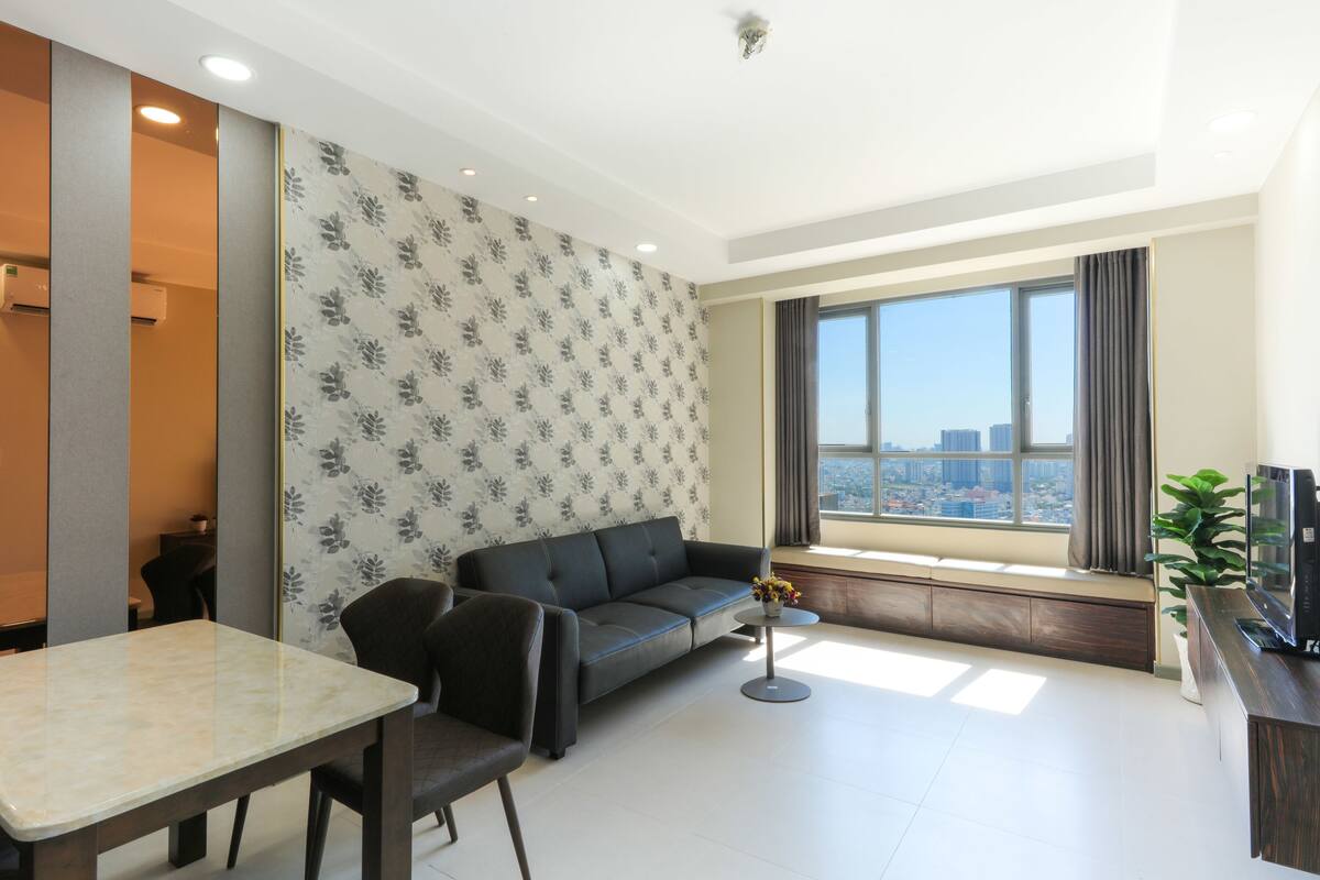 A modern living room with a sofa, a dining table, and a large window offering a city view.
