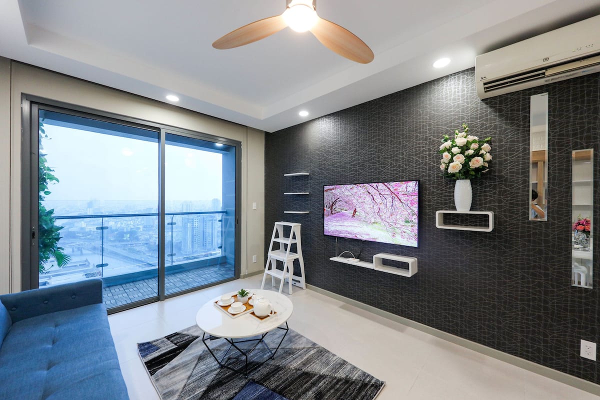 A modern living room with a large window, a flat-screen TV, a ceiling fan, and a small table with a tray of items.