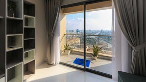 Une chambre d’hôtel moderne dotée d’un grand balcon, offrant une vue sur la ville, et comprenant une bibliothèque intégrée.