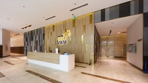 Un comptoir d'accueil avec une enseigne indiquant « The Gold View », situé dans un hall d'entrée moderne doté d'un sol carrelé et d'un mur décoratif en bois.