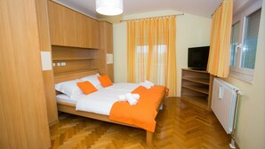 Ein Schlafzimmer mit einem hölzernen Bett, orangefarbener Bettwäsche, einem Fernseher und einem Fenster mit Vorhängen.