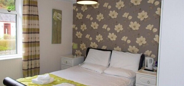 Habitación de hotel con cama, mesita de noche, lámpara y ventana con cortinas.
