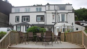 A two-story building with a wooden deck and outdoor seating area. - Lochside Guest House (Arrochar)