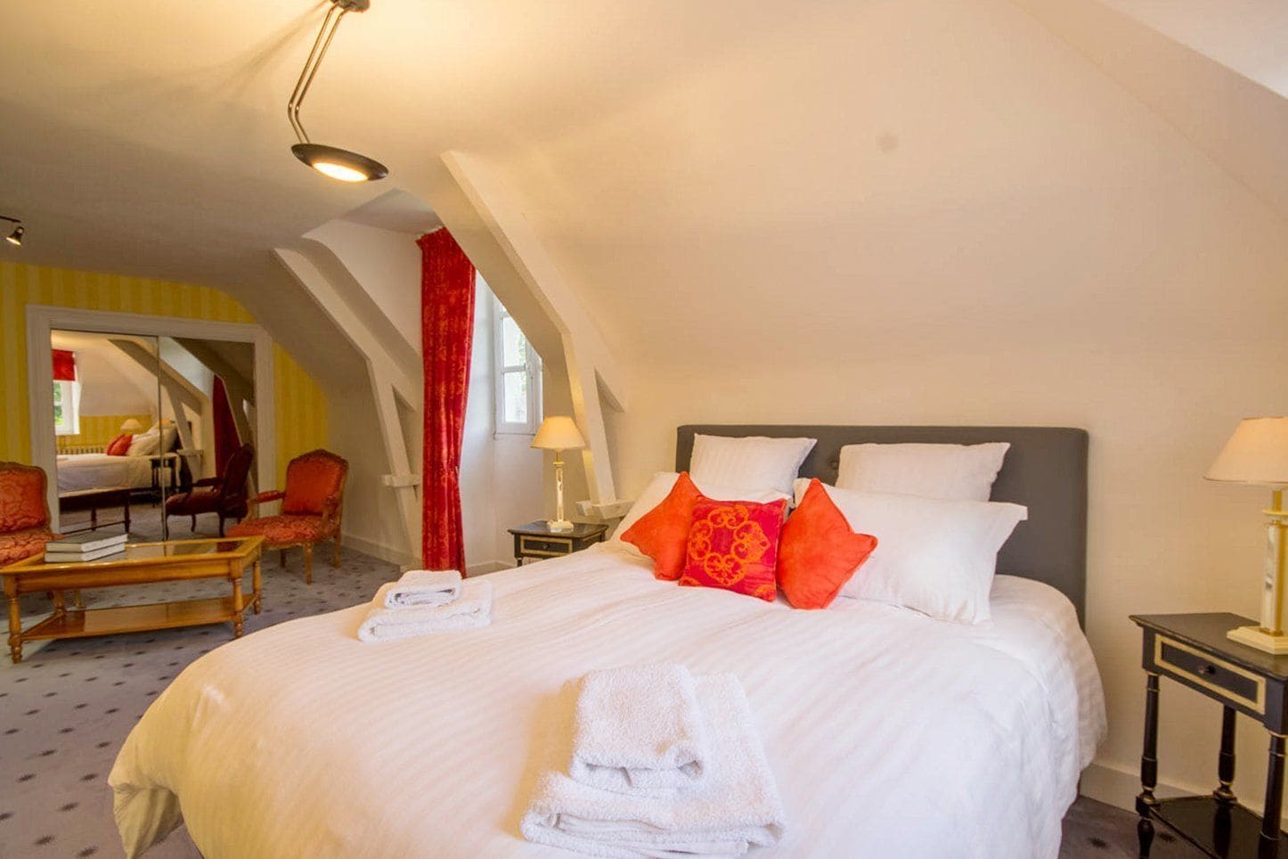 Una camera d'albergo con un letto grande, due comodini, una sedia, uno specchio e una finestra con tende rosse.