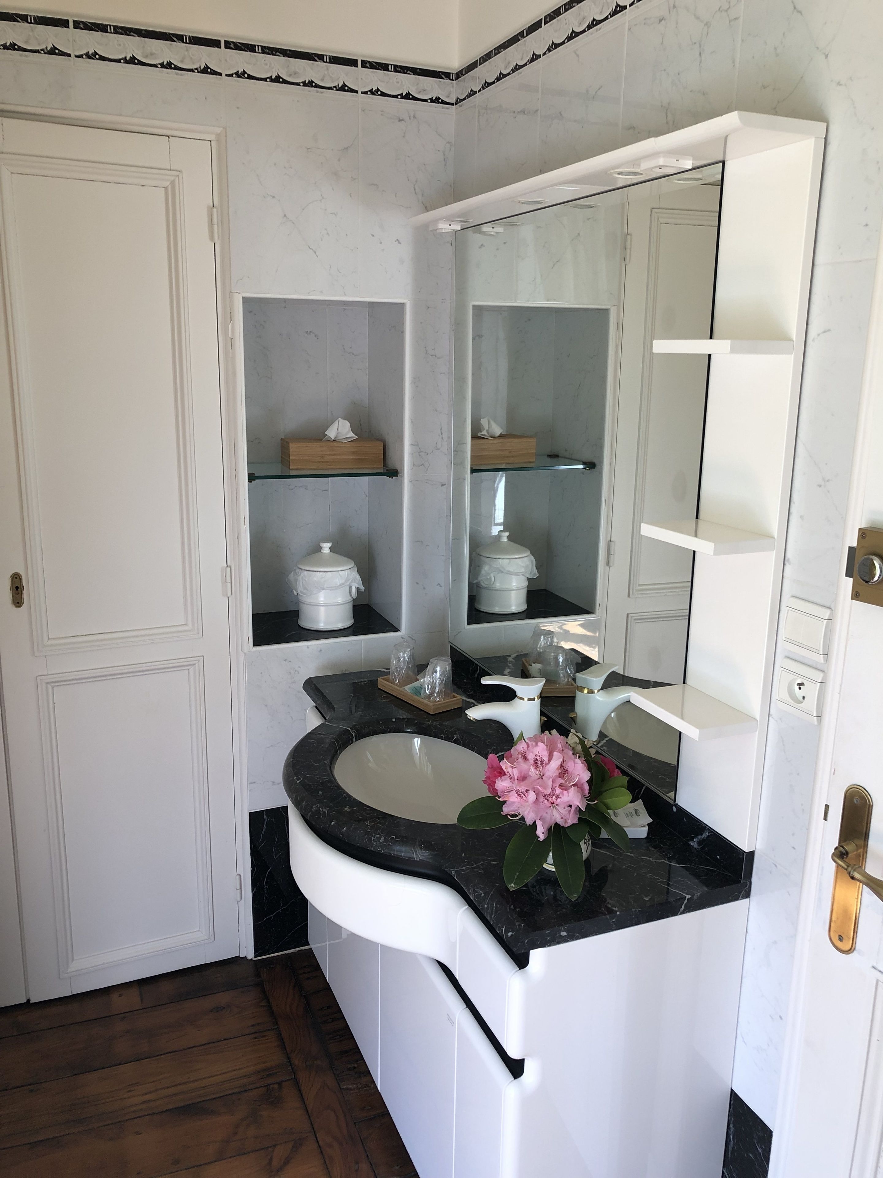 A bathroom with a white vanity, a large mirror, and a marble backsplash.