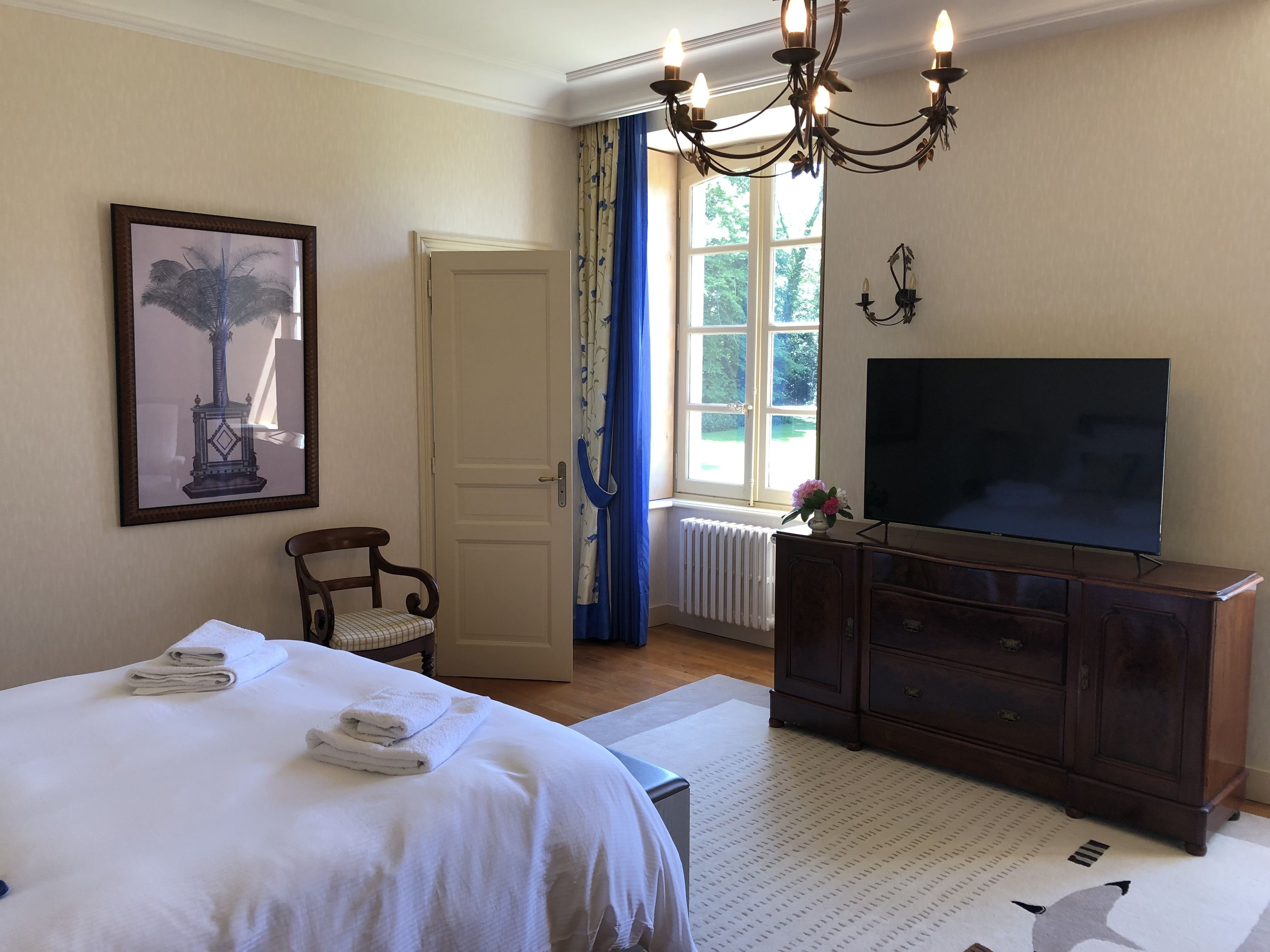 Una habitación de hotel con cama, televisor, cómoda, silla y ventana con cortinas.