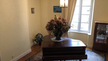 A piano in a room with a window, a vase of flowers, and a patterned rug.