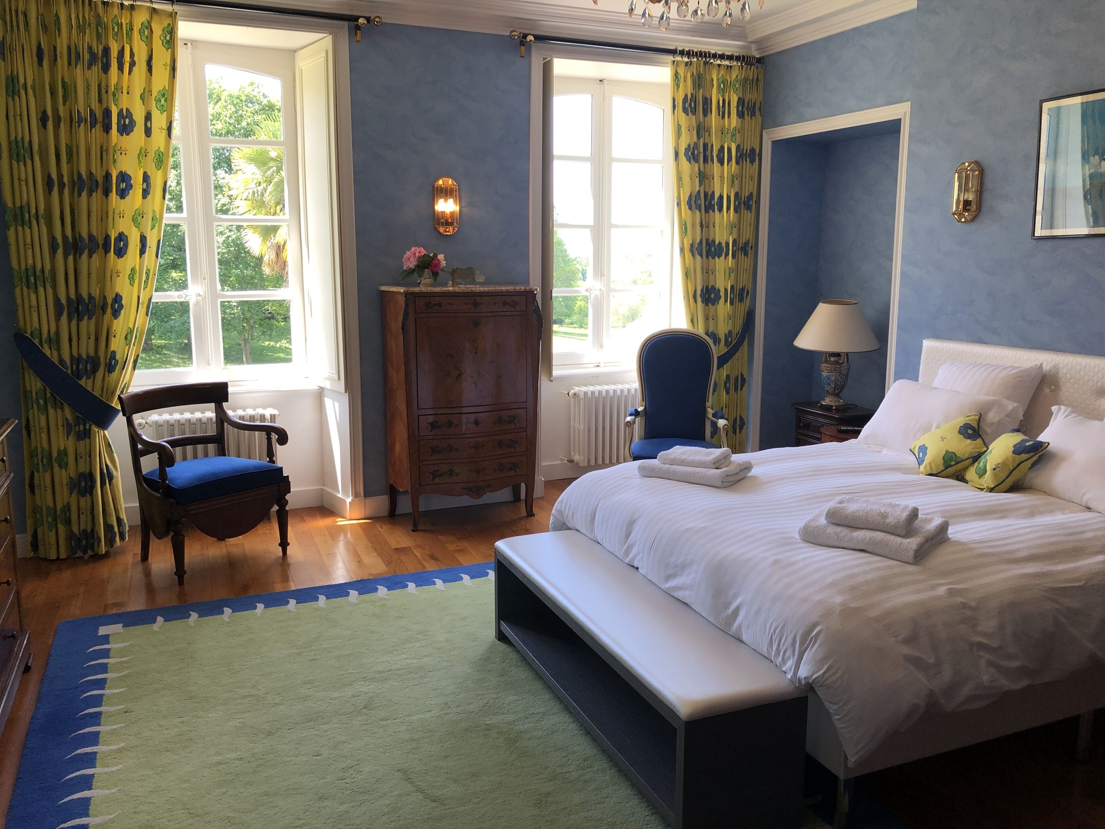 A bedroom with a bed, a chair, a dresser, and a window with curtains.