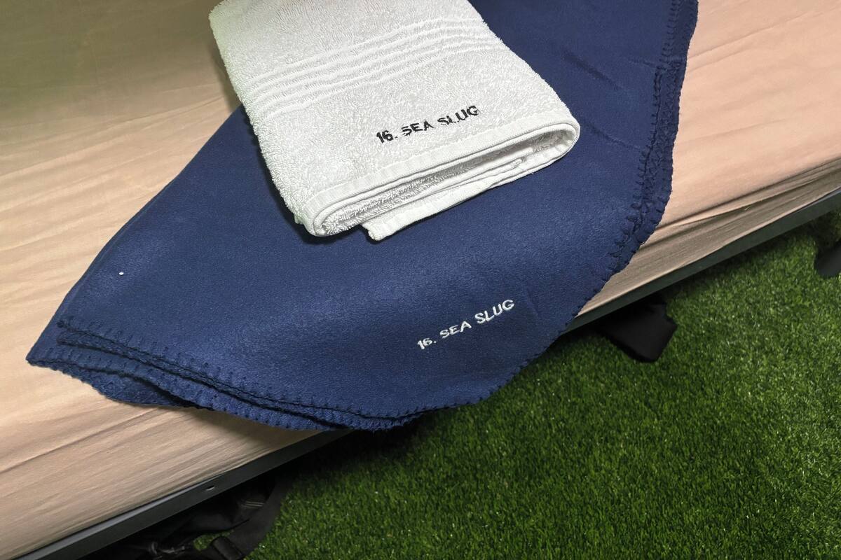 Een netjes gevouwen witte handdoek met de tekst '16 SEA SLUG', geplaatst op een blauwe handdoek op een houten bankje.