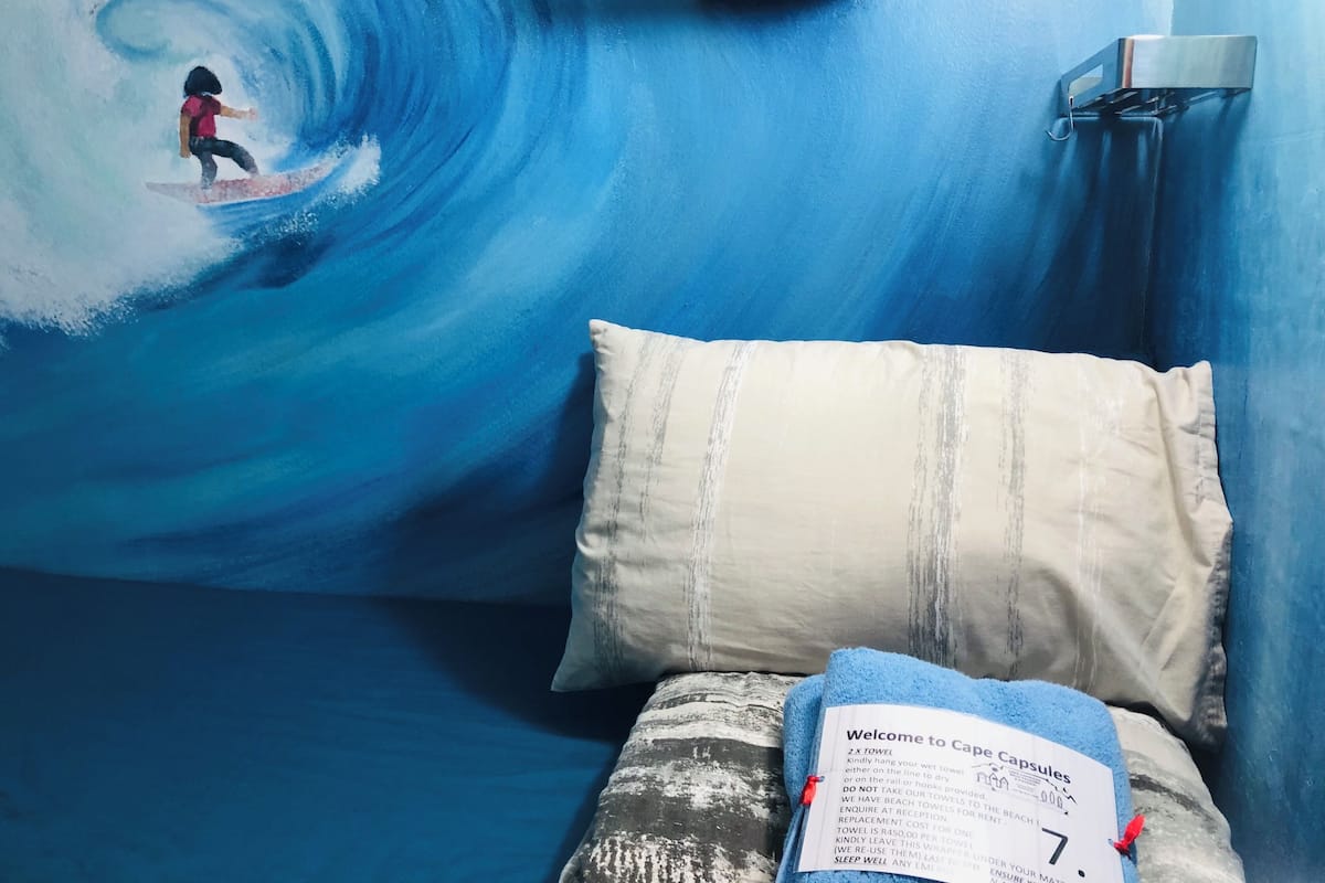 Een kamer met een muurschildering van een surfer op een golf, een bed met een kussen, en een bord aan de muur.