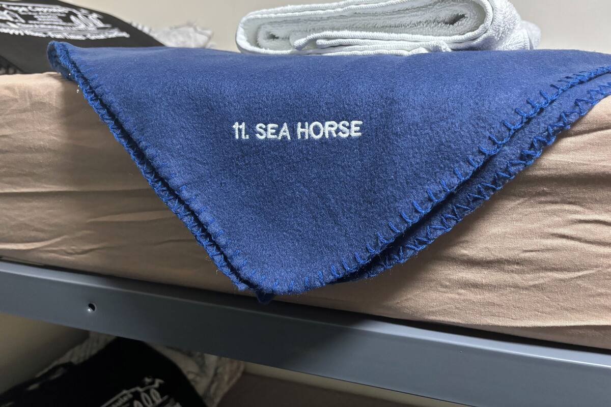 Een blauwe handdoek met de tekst 'SEA HORSE' erin geborduurd, ligt op een bed.