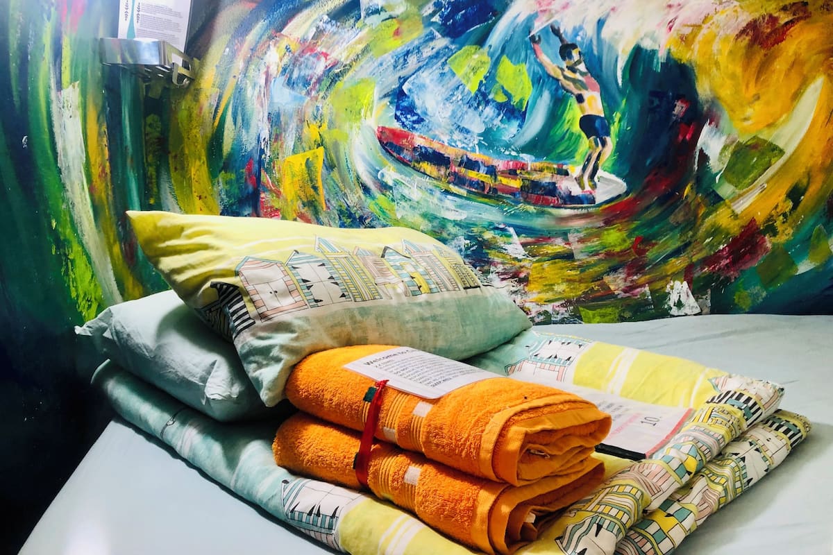Een bed met kussens en opgerolde handdoeken, een schilderij aan de muur en een menukaart.