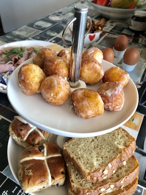 Ein Teller mit glasieren Doughnuts, ein Teller mit Brötchen und ein Laib geschnittenes Brot auf einem Tisch.