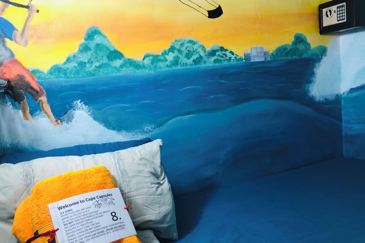 Een kamer met een muurschildering van een strand, een bed met een kussen, en een bord met regels over handdoeken en dekens.