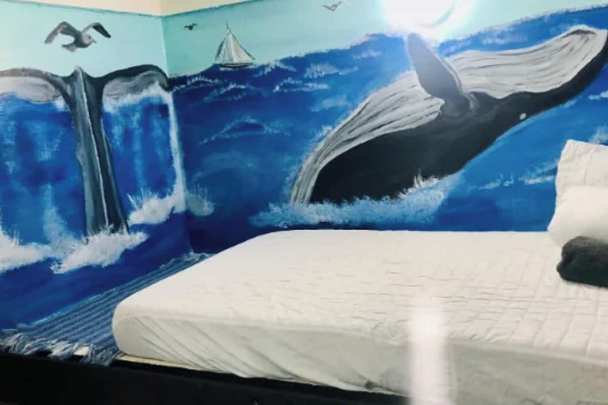 Een kamer met een muurschildering van een walvis en golven, een bed met wit beddengoed en een kussen.