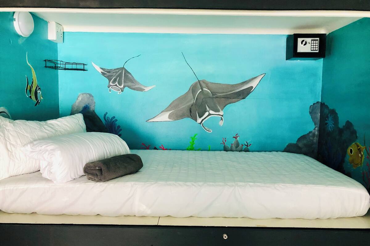 Een bed met witte beddengoed, een zwart hoofdeinde en een muurschildering van vliegende manta roggen.