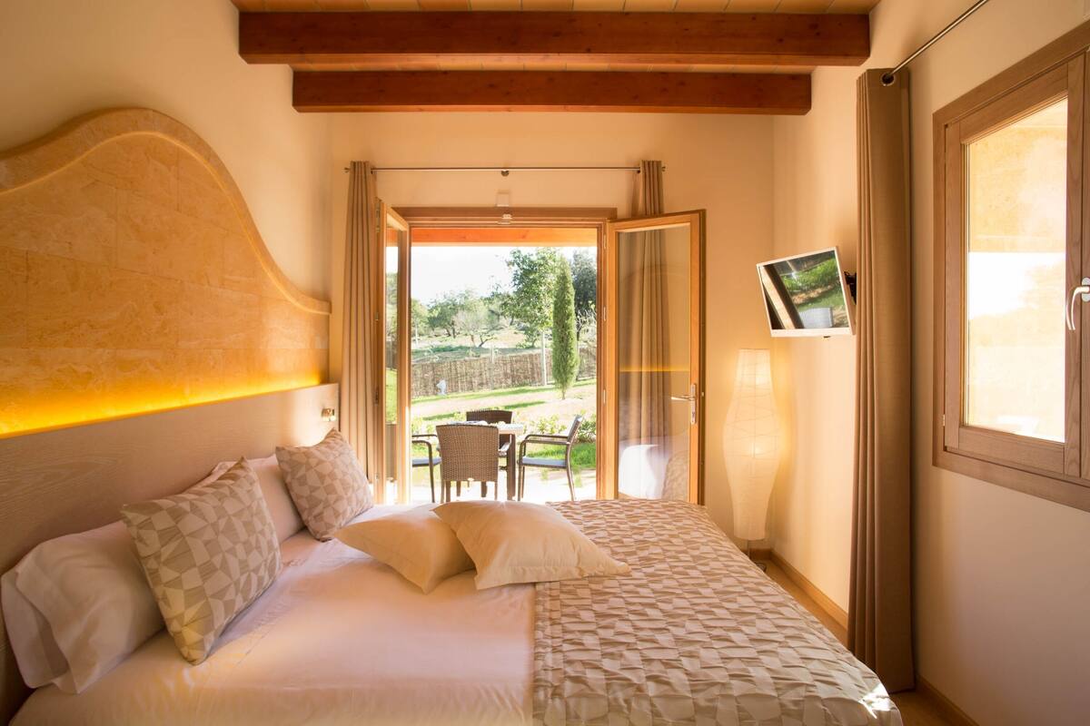 A bedroom with a bed, a TV mounted on the wall, and a view of the outdoors.