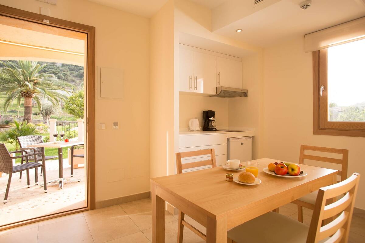A dining area with a table set for two, a coffee maker, and a plate of fruit.
