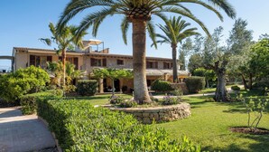 A two-story stone building with a garden featuring palm trees and well-maintained lawns.