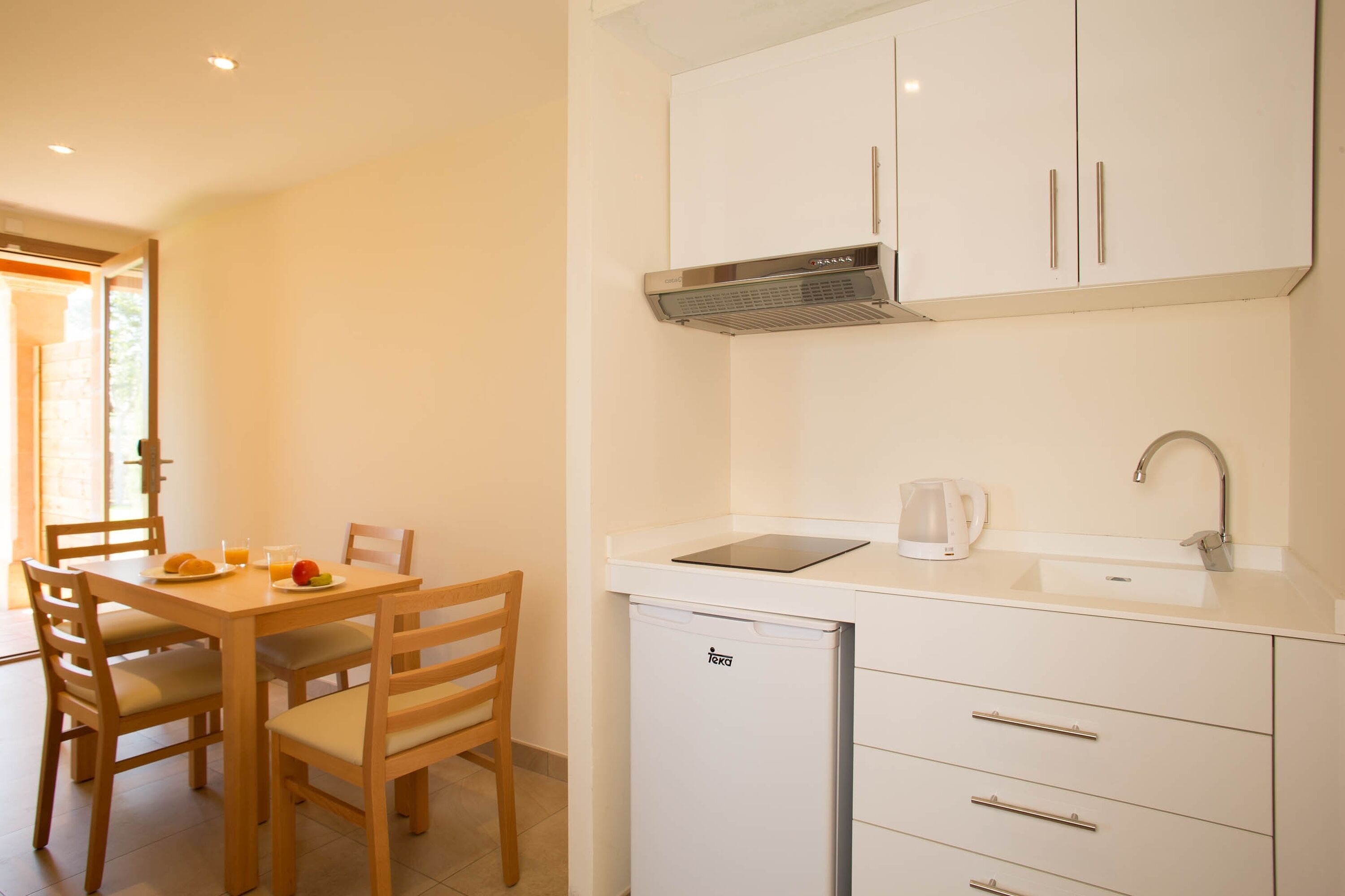 A compact kitchen with white cabinets, a built-in dishwasher, and a dining area with a wooden table and chairs.