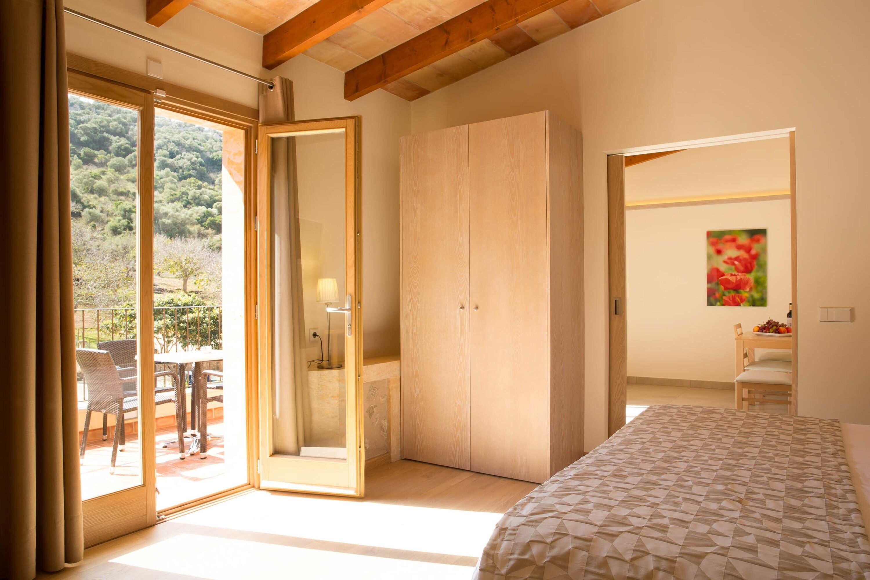 Un dormitorio con una cama grande, un armario y un ventanal corredera que da a un patio exterior con sillas y una mesa.