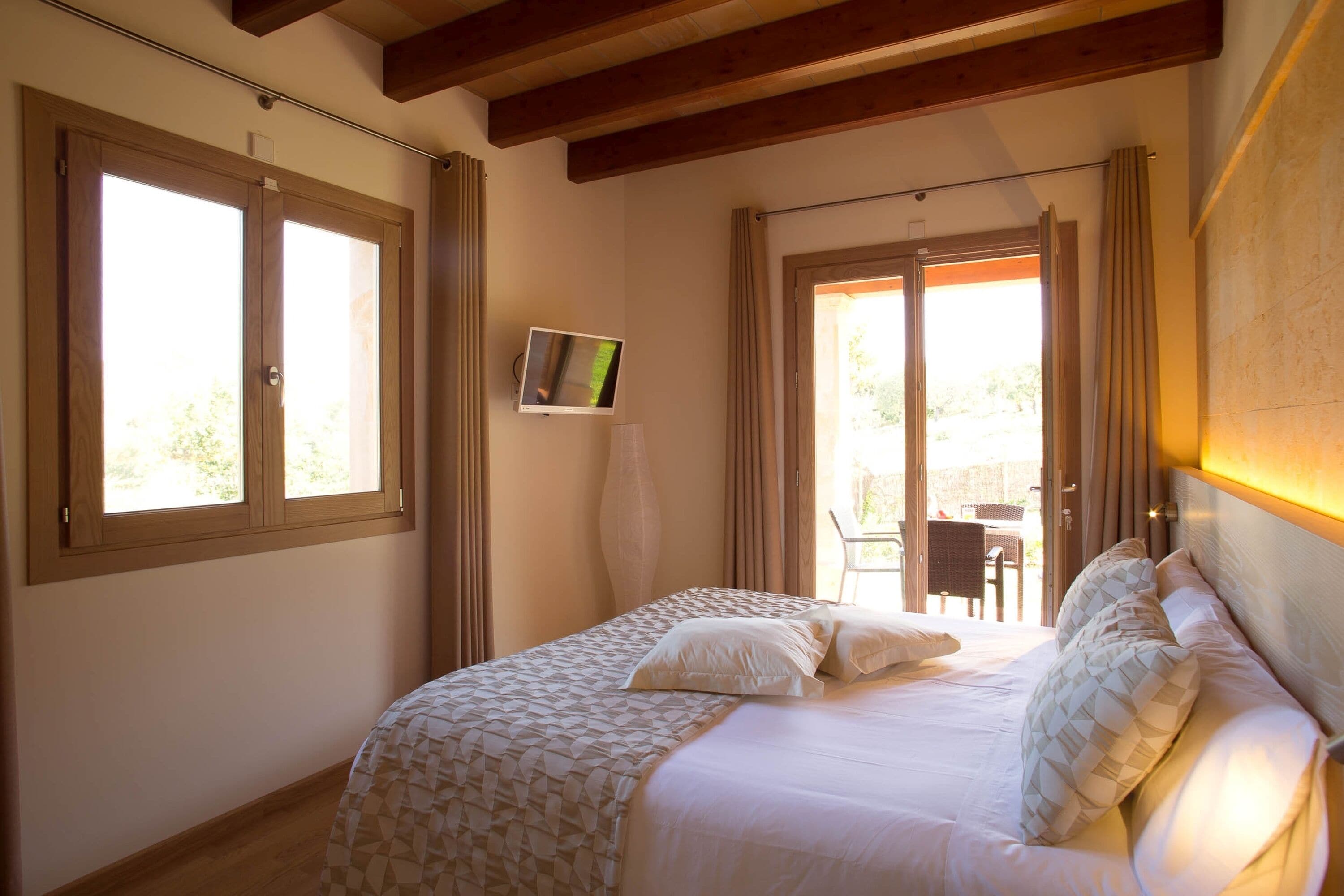 A bedroom with a large bed, a television on the wall, and a view of the outside through a sliding door.