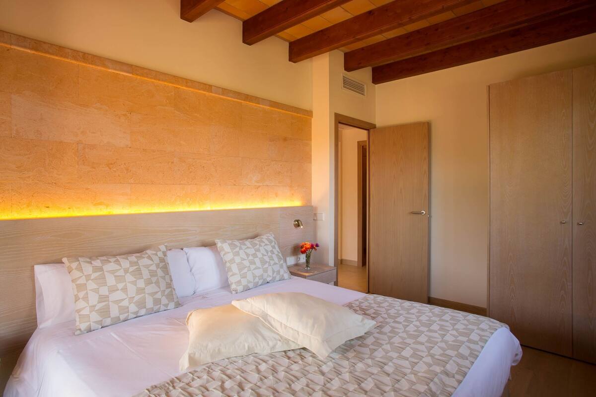 A neatly made bed with patterned bedding, a bedside table with a vase of flowers, and a wooden wardrobe.