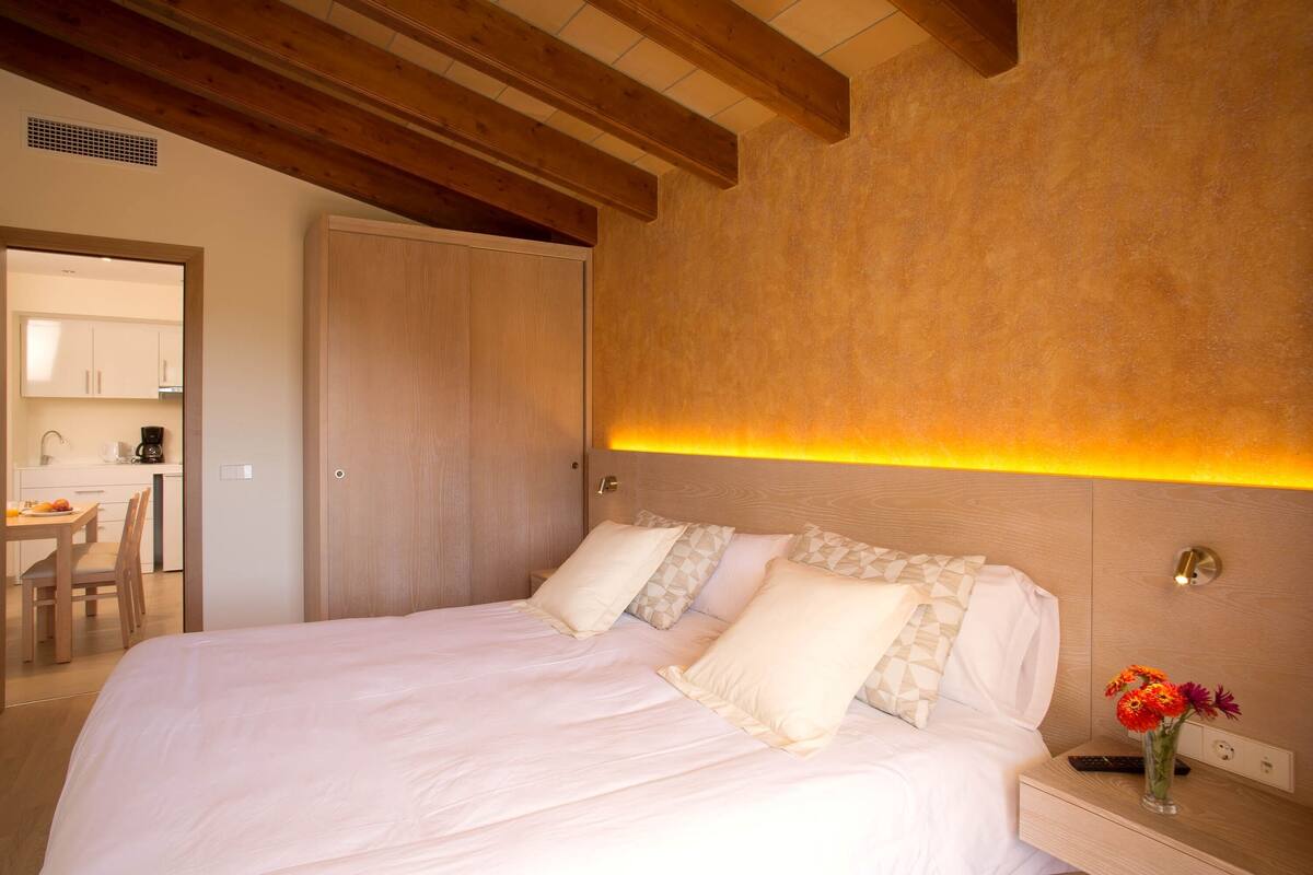 A bedroom with a bed, bedside table, and a nightstand with a vase of flowers.
