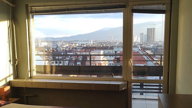 Un dormitorio con un ventanal grande que da a una vista panorámica de la ciudad y una montaña.
