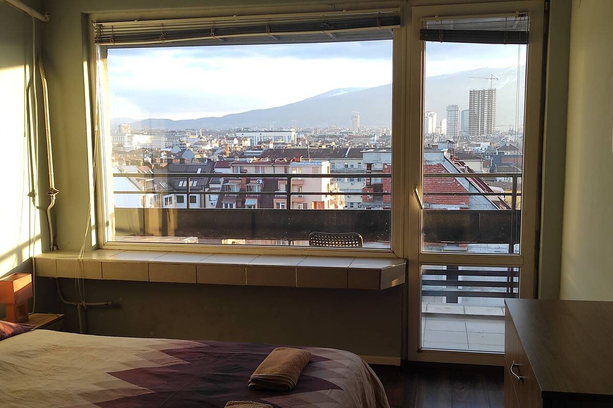 A bedroom with a large window overlooking a cityscape and a mountain.