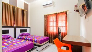A room with two beds, a desk, an orange chair, and a mirror. - Trans Bandara Residence by Zuzu (Deli Serdang)