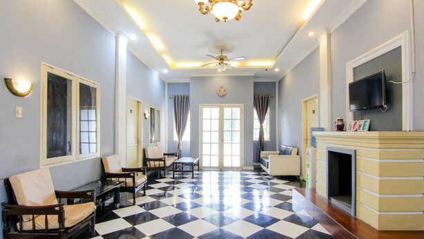 A hotel lobby with a checkered floor, seating area with chairs and sofas, a fireplace, and a television mounted on the wall. - Trans Bandara Residence by Zuzu (Deli Serdang)