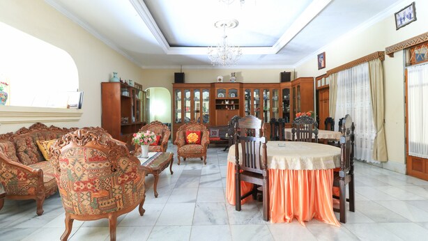 A spacious living room with a dining table, ornate chairs, and a large cabinet. - Andrin Daspatt Hotel (Makassar)