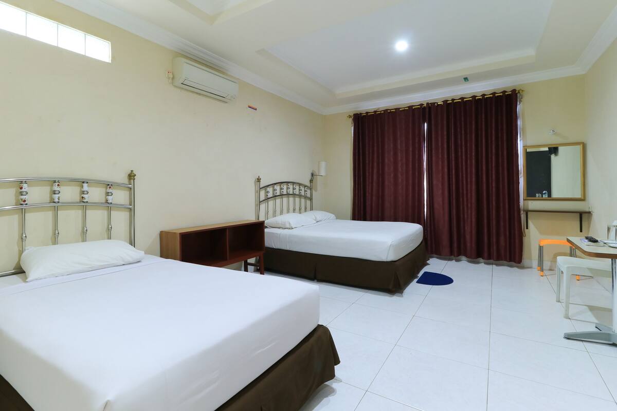 A hotel room with two beds, a desk, a chair, a mirror, and a window with curtains.