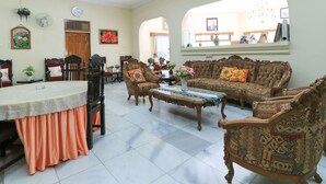A spacious living room with a dining area, featuring a chandelier, a clock, and a large window with an arched view. - Andrin Daspatt Hotel (Makassar)