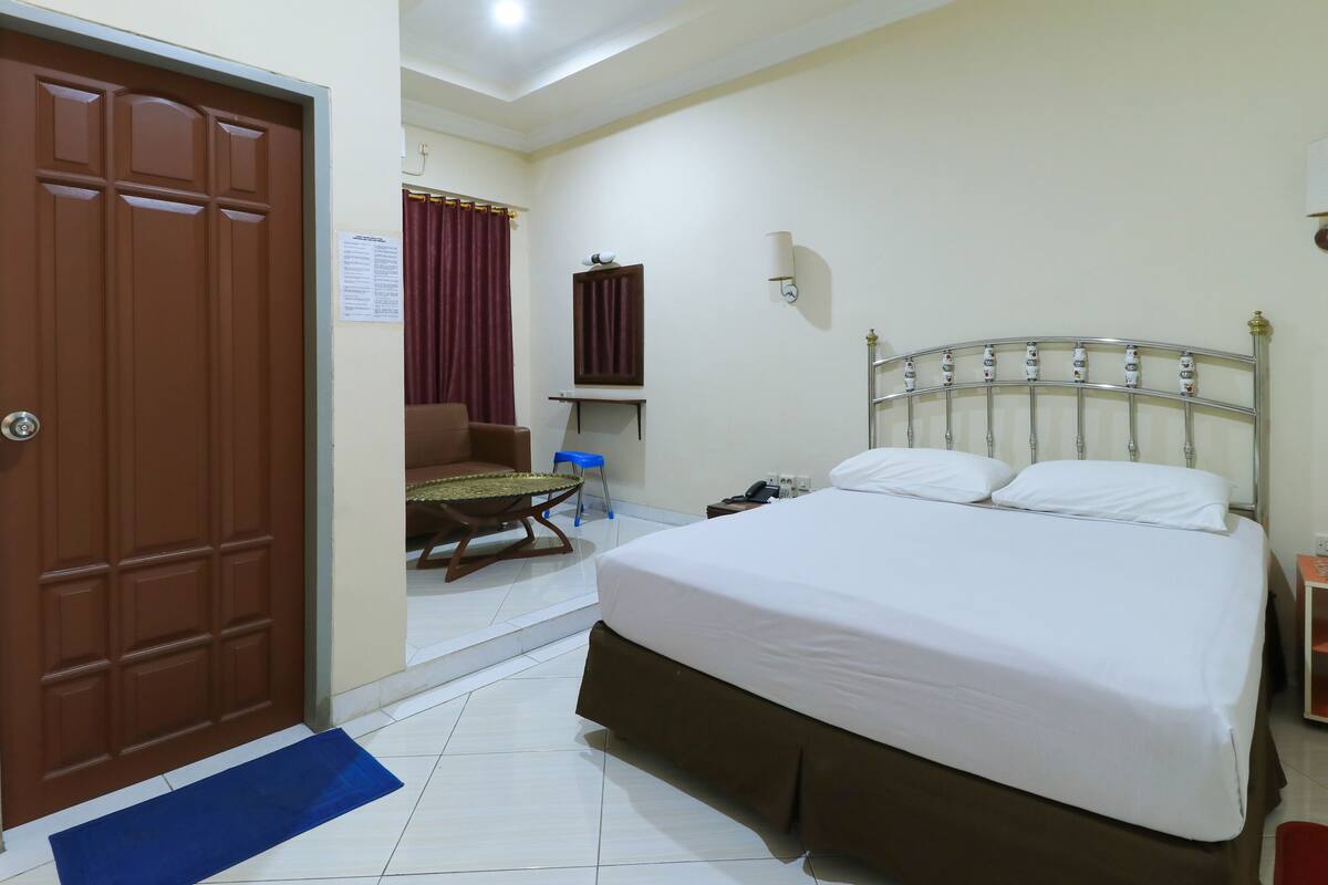 A hotel room with a large bed, a desk, a chair, and a wardrobe.