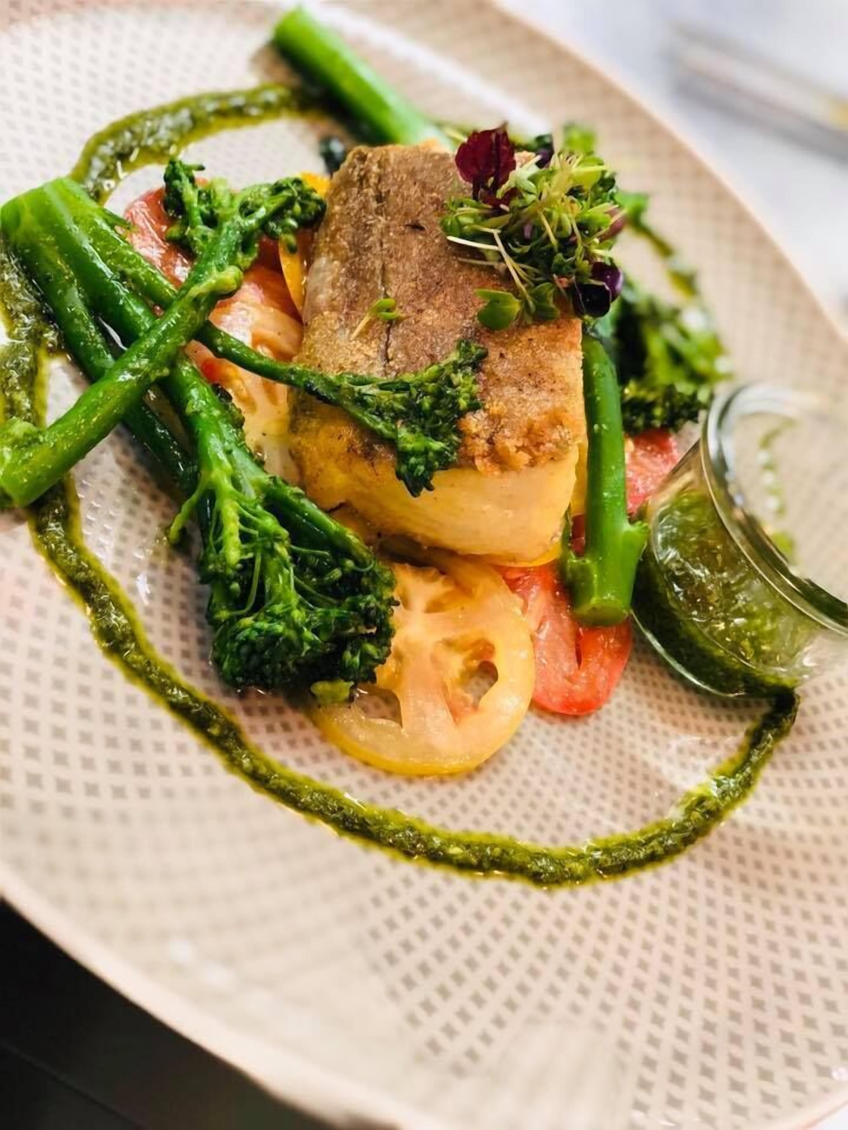A plate of food with a piece of fish, green vegetables, and a sauce.