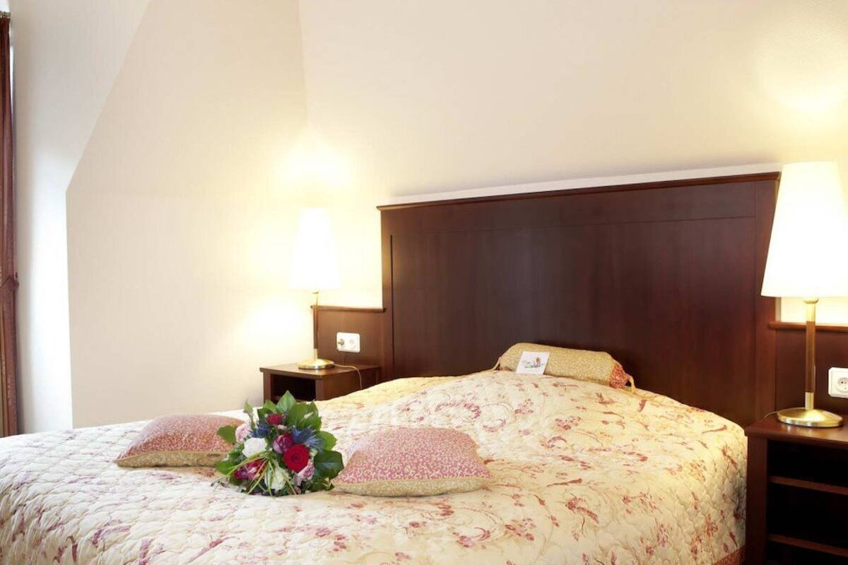 A neatly made bed with floral bedding, two bedside lamps, and a bouquet of flowers.