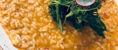 Un plato de risotto adornado con tomates cherry y una rodaja de rábanos, servido en un plato moteado.